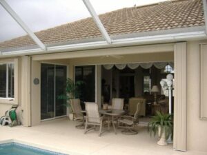 Accordion shutters open in backyard, showing covered patio beside a pool.