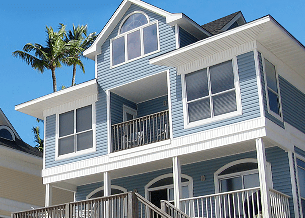 Light blue three-story home with white trim and palm trees in background.