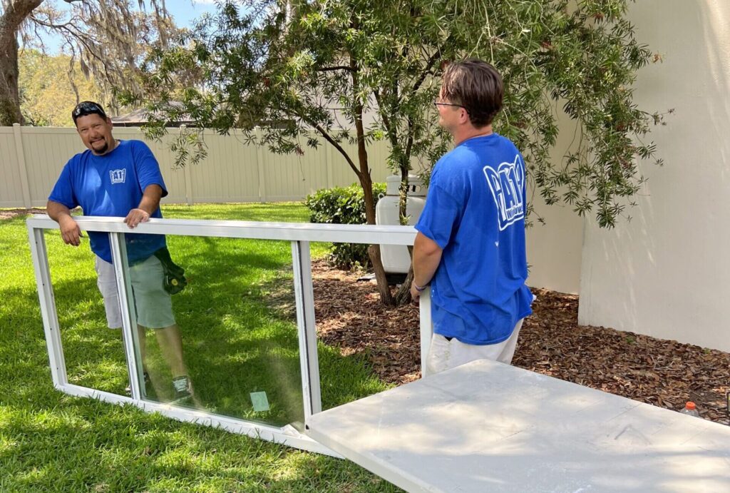 A1 Windows & Doors installers carrying a large window in a home's backyard.