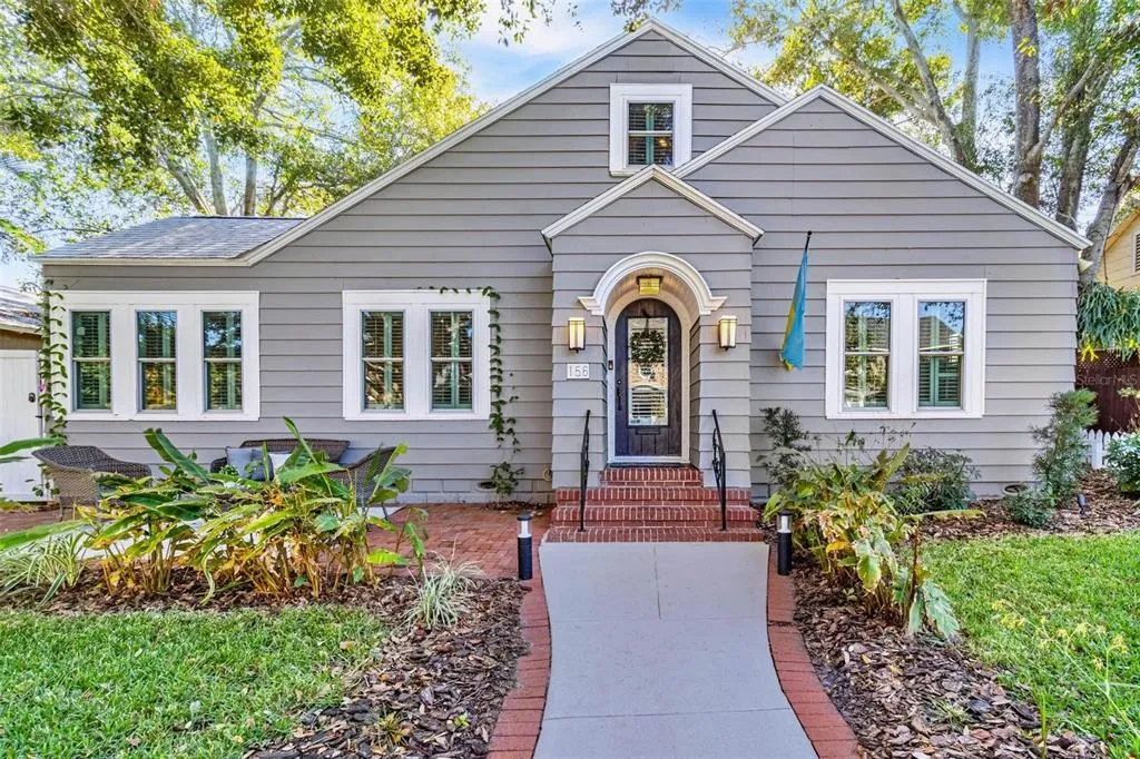Front view of a small light gray home with a newly replaced front door in Tampa, FL. Brick front steps and small brick patio to the left.