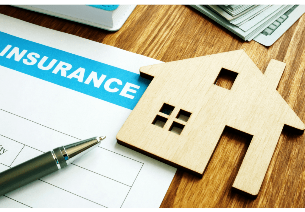 Small wooden home cutout next to an insurance paper and a pen